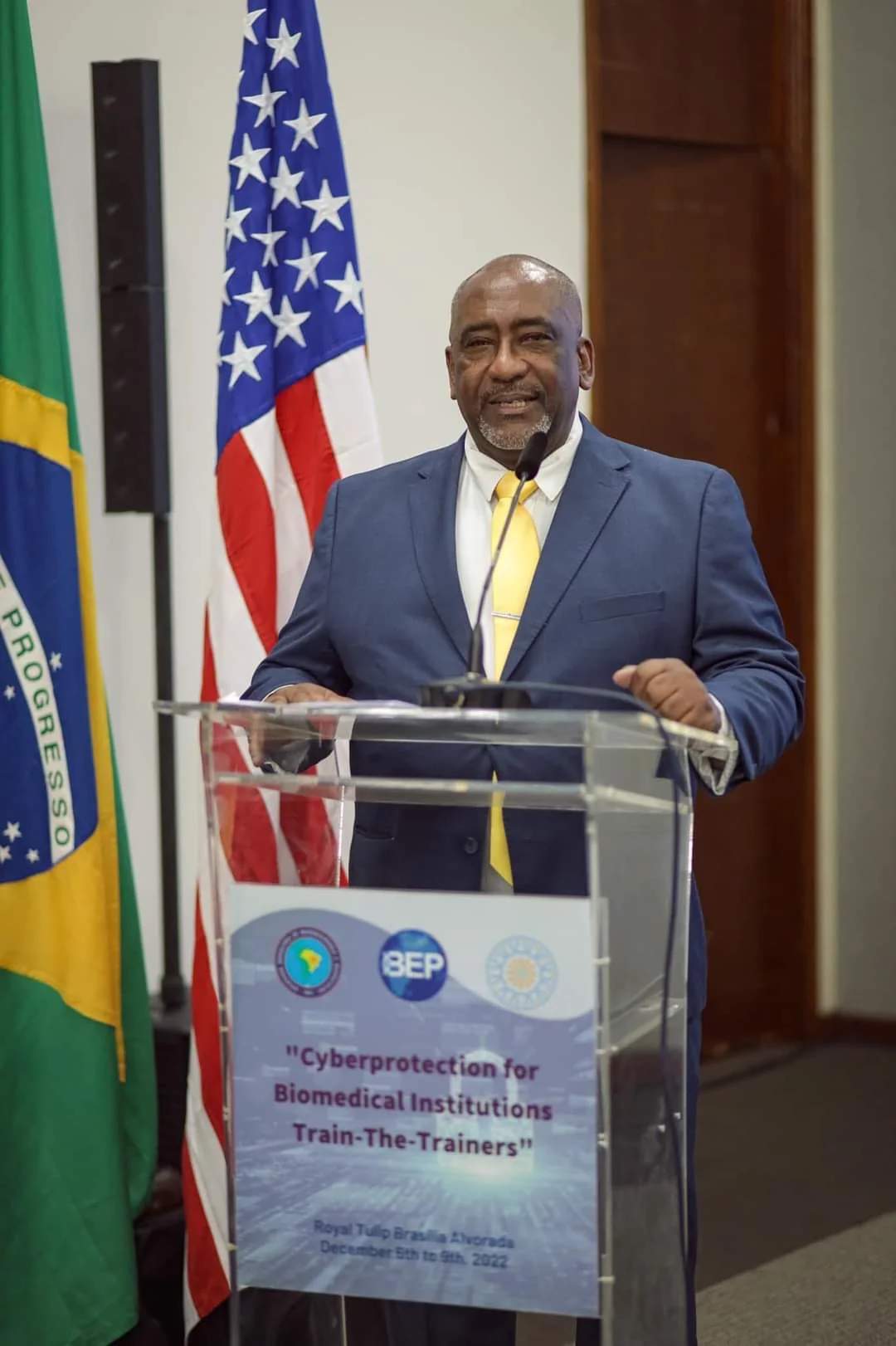 Walter diante das bandeiras brasileira e americana em evento institucional